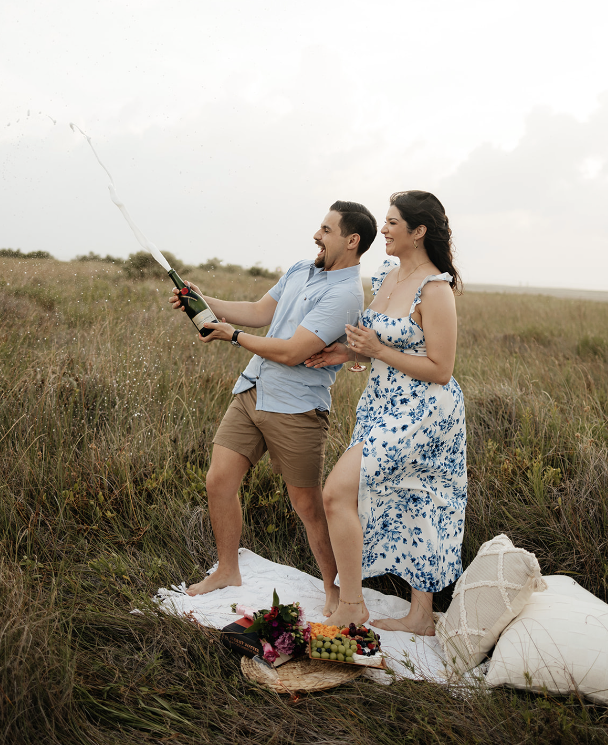 Engaged couple sitting on a picnic blanket, laughing and enjoying a romantic outdoor engagement session captured by San Antonio photographer Angie Rich.