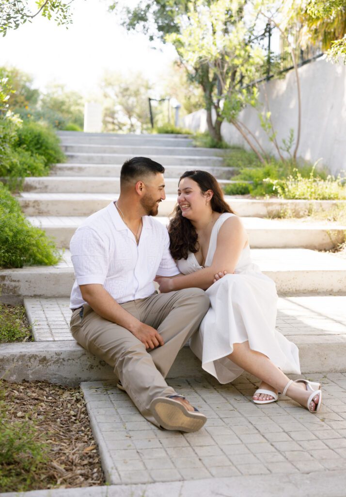 Couple laughing together on the garden steps during an engagement session at the San Antonio Botanical Garden in San Antonio, Texas.
