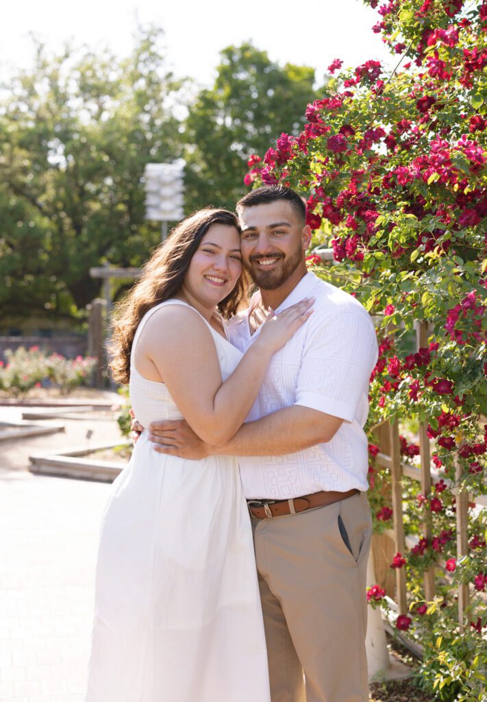 Couple embracing beside blooming flowers during a spring engagement session at the San Antonio Botanical Garden.