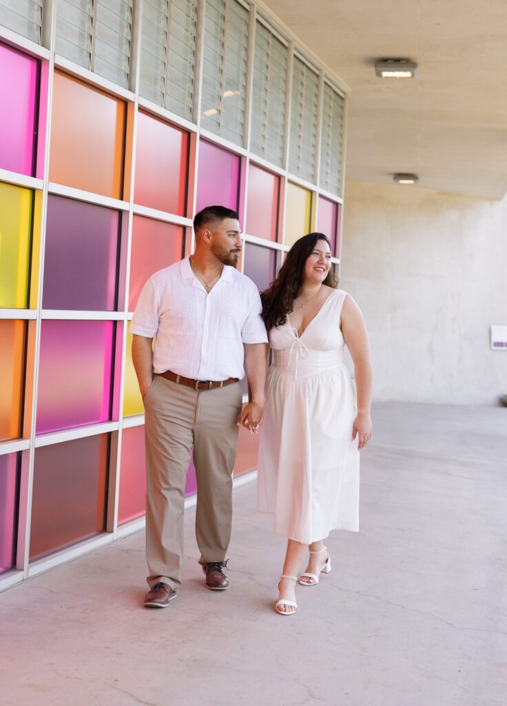 Couple walking beside the colorful glass walls during their engagement session at the San Antonio Botanical Garden.